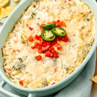 square image of 15-minute jalapeno spinach & artichoke dip topped with red bell pepper and jalapeno in a casserole dish