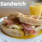 bacon, egg waffle sandwich on white plate with glass of orange juice