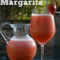 strawberry margarita in a pitcher and glass garnished with strawberry