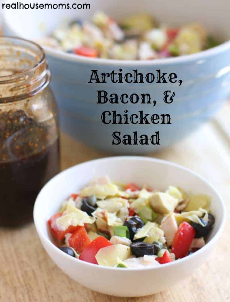 artichoke, bacon & chicken salad in a white bowl with dressing in mason jar