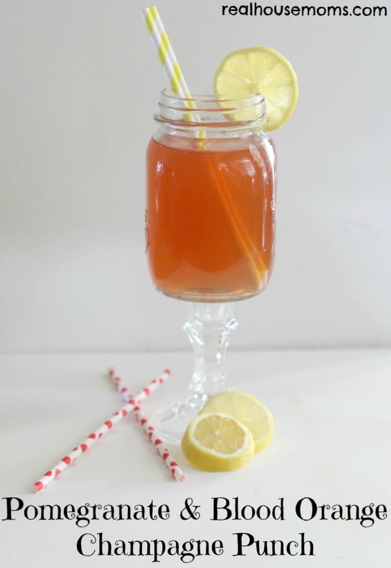 pomegranate and blood orange champagne punch in a stemmed glass with lemon slice