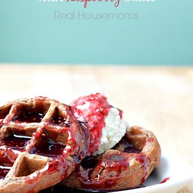 chocolate waffles stacked on a plate and topped with strawberry sauce