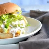 fish fillet sandwich topped with shredded lettuce and tartar sauce on a white plate