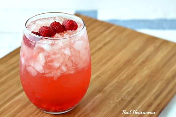 spiked raspberry mango strawberry lemonade in a glass with raspberry garnish