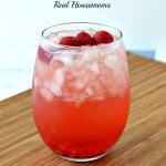 spiked raspberry mango strawberry lemonade in a glass with raspberry garnish