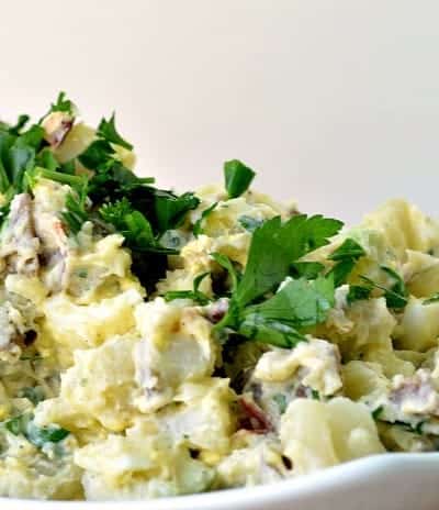 Best ever potato salad garnished with parsley served in a white serving bowl