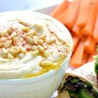 Super Creamy Hummus in a bowl served with carrot sticks and vegetable wrap
