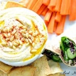Super Creamy Hummus in a bowl served with carrot sticks, chips, and vegetable wrap