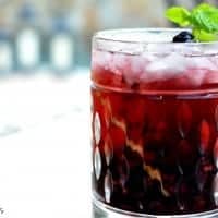 A Spiced Blackberry Cocktail served in a Old fashioned glass garnished with a mint mint leave and a black berry on the rocks