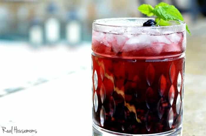 A Spiced Blackberry Cocktail served in a Old fashioned glass garnished with a mint mint leave and a black berry on the rocks