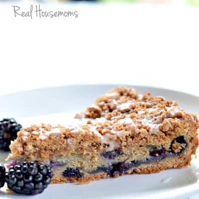 Slice of Very Berry Coffee Cake displayed on a white sharing plate topped with blueberries