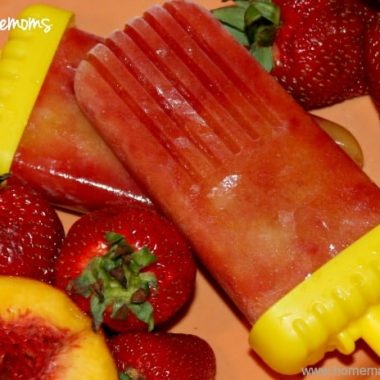 Strawberry peach popsicles on orange plate surrounded bystrawberries and peaches