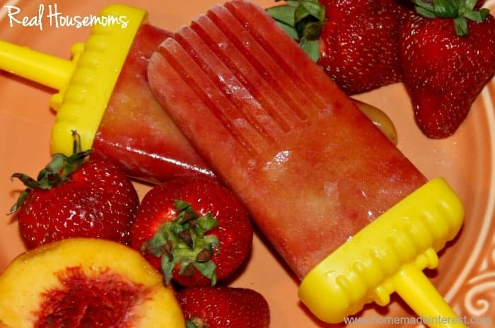 Strawberry peach popsicles on orange plate surrounded bystrawberries and peaches