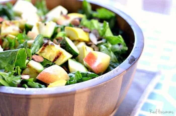 Summer Bounty Salad topped with sliced apples served in a wooden bowl