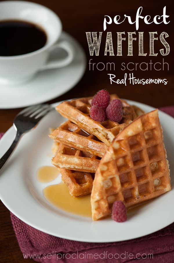 Perfect Waffles from Scratch topped with resberries and drizzled in syrup served on a white sharing dish Coffee displayed in background of photo