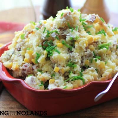 Warm Bacon Corn Smashed Potato Salad served in red baking dish