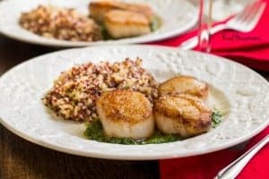 Pan Seared Scallops with creamy pesto sauce served on a white dish served with a side of rice