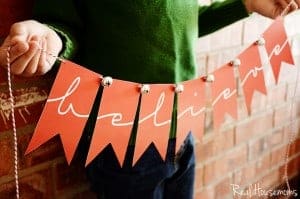Printable believe banner, child holding banner, Banner is red with red and white string with bells at the top