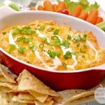 Creamy Buffalo Ranch Chicken Dip served in a red and white baking dish with a side of chips, carrots and celary
