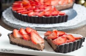 Strawberry Chocolate Tart topped with sliced strawberries, two slices displayed on a serving dish with tart in background