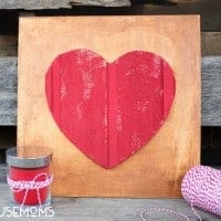DIY Wood Heart Art. Wood plaque with wood red painted heart in he middle. Red candle off to the side of the photo with a white and red string as a bow.