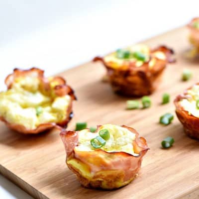 Ham Swiss and Egg cups topped with chives served on a cutting board