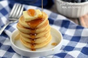 Silver dollar pancakes. five minni pancakes stacked on top of each other drizzled with syrup and toped with butter. Blueberries on the side