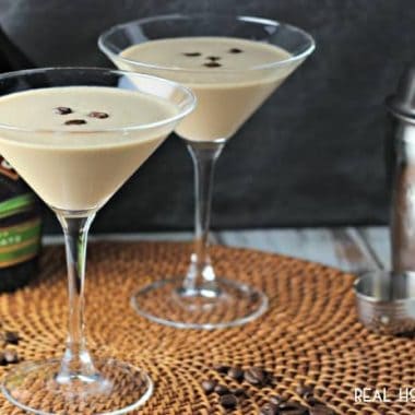 Bailey's Flat White Martini. Cocktail is served in two Martini glasses arnished with three coffee beans. Cocktail shaker is off to the side of photo