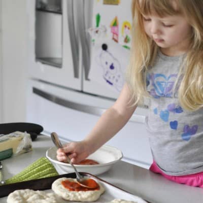 Bread maker pizza dough. little girl topping Mini pizza's with tomato sauce