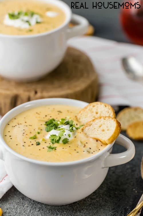 soup bowls filled with Slow Cooker Broccoli Cheese Soup, served with toasts and topped with sour cream, parsley, and pepper