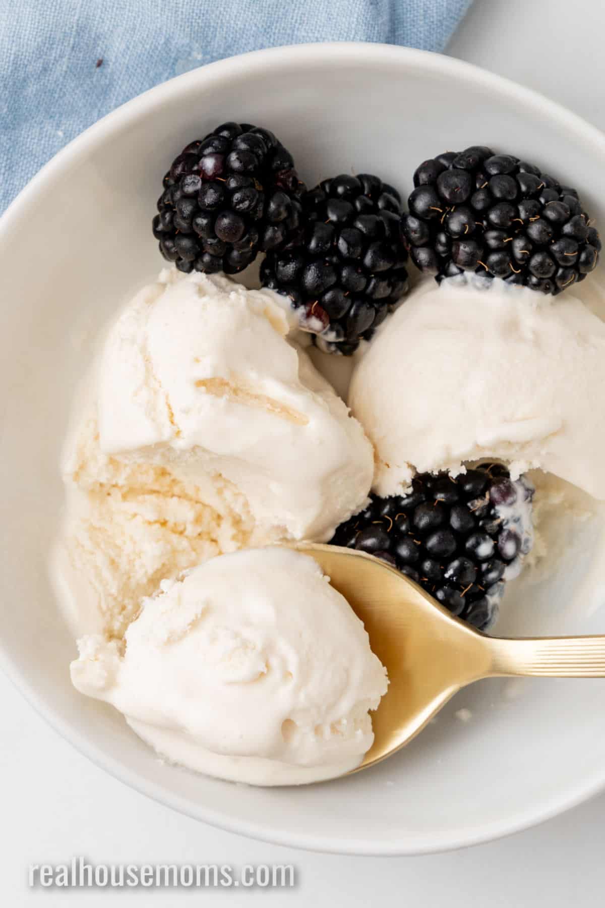 bite of keto ice cream on a spoon resting in the bowl with ice cream and fresh blackberries