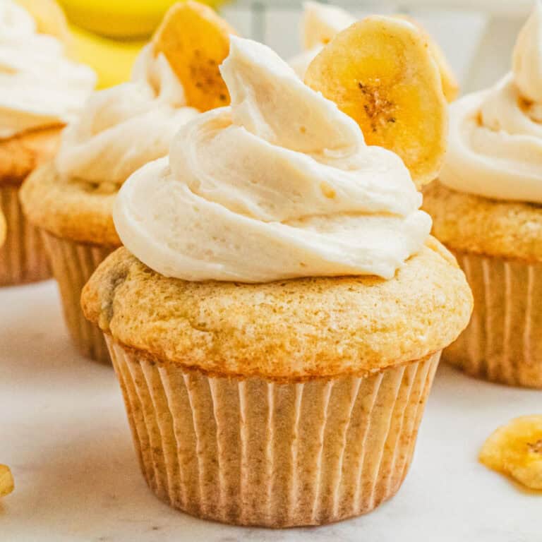 square image of banana cupcakes frosted with buttercream and garnished with a banana chip