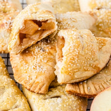 square image of air fryer apple hand pies piled on a wire rack with one broken in half to show filling