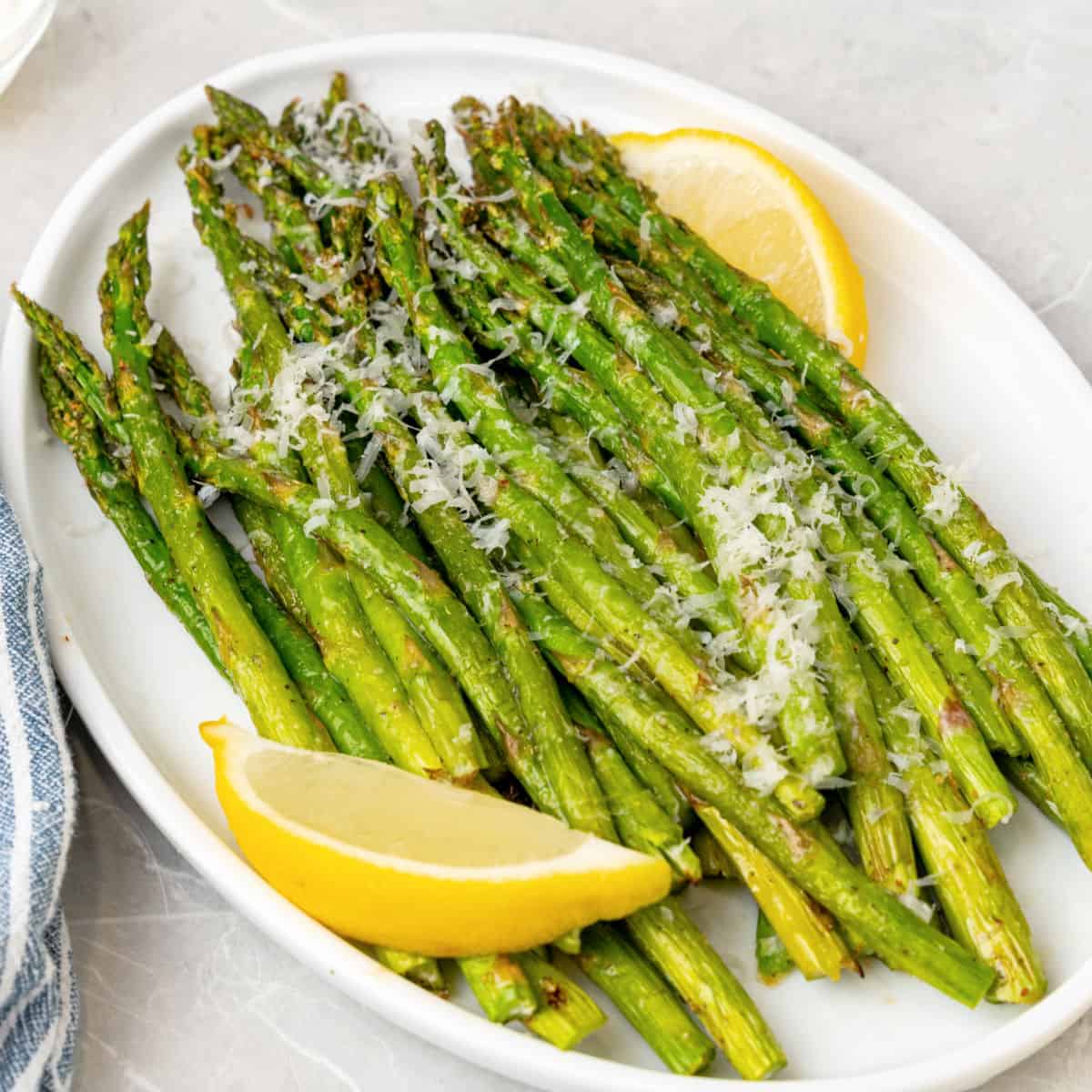 square image of air fryer asparagus topped with parmesan on platter with lemon wedges