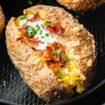 square image of a loaded air fryer backed potato in an air fryer basket