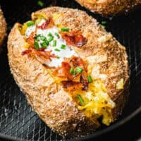 square image of a loaded air fryer backed potato in an air fryer basket