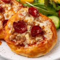 close up square image of air fryer biscuit pizzas on a plate with a salad