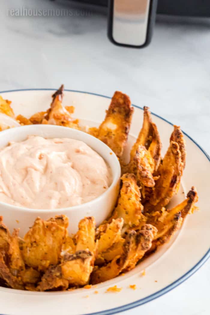 air fryer blooming onion in a serving bowl with a ramekin of dip in the middle