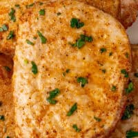 image of air fryer boneless pork chop topped with parsley on a dinner plate with side dishes with the title of the post on top with pink and black lettering