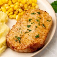 air fryer boneless pork chop topped with parsley on a dinner plate with side dishes