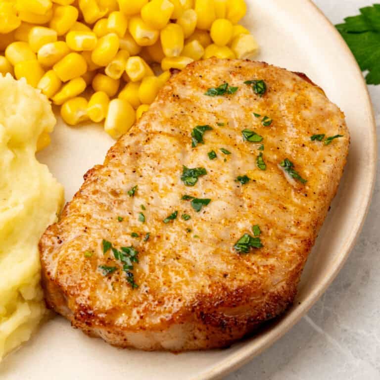 air fryer boneless pork chop topped with parsley on a dinner plate with side dishes