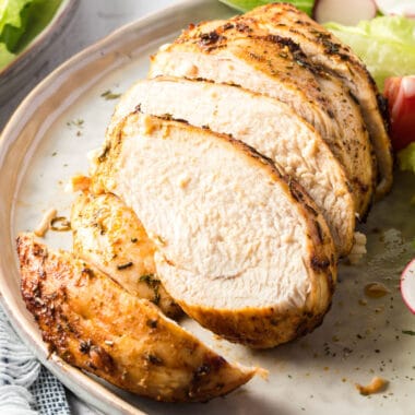 square close up image of sliced air fryer chicken breast on a plate with salad