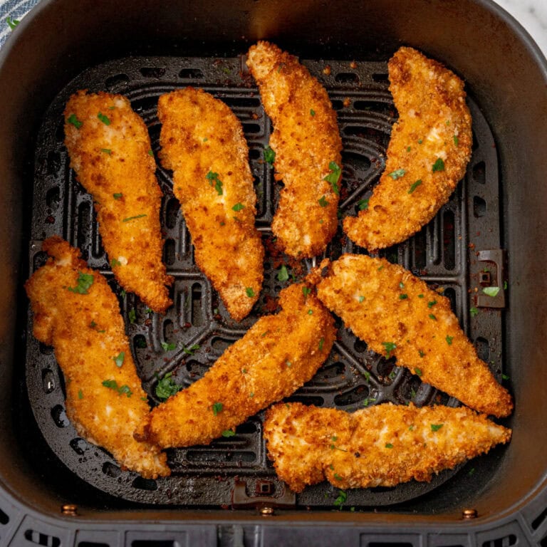 square image of air fryer chicken tenders topped with chopped parsley in the air fryer basket