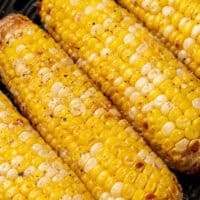 image of cooked air fryer corn on the cob in the air fryer basket, with the title of the post on top in pink and black lettering
