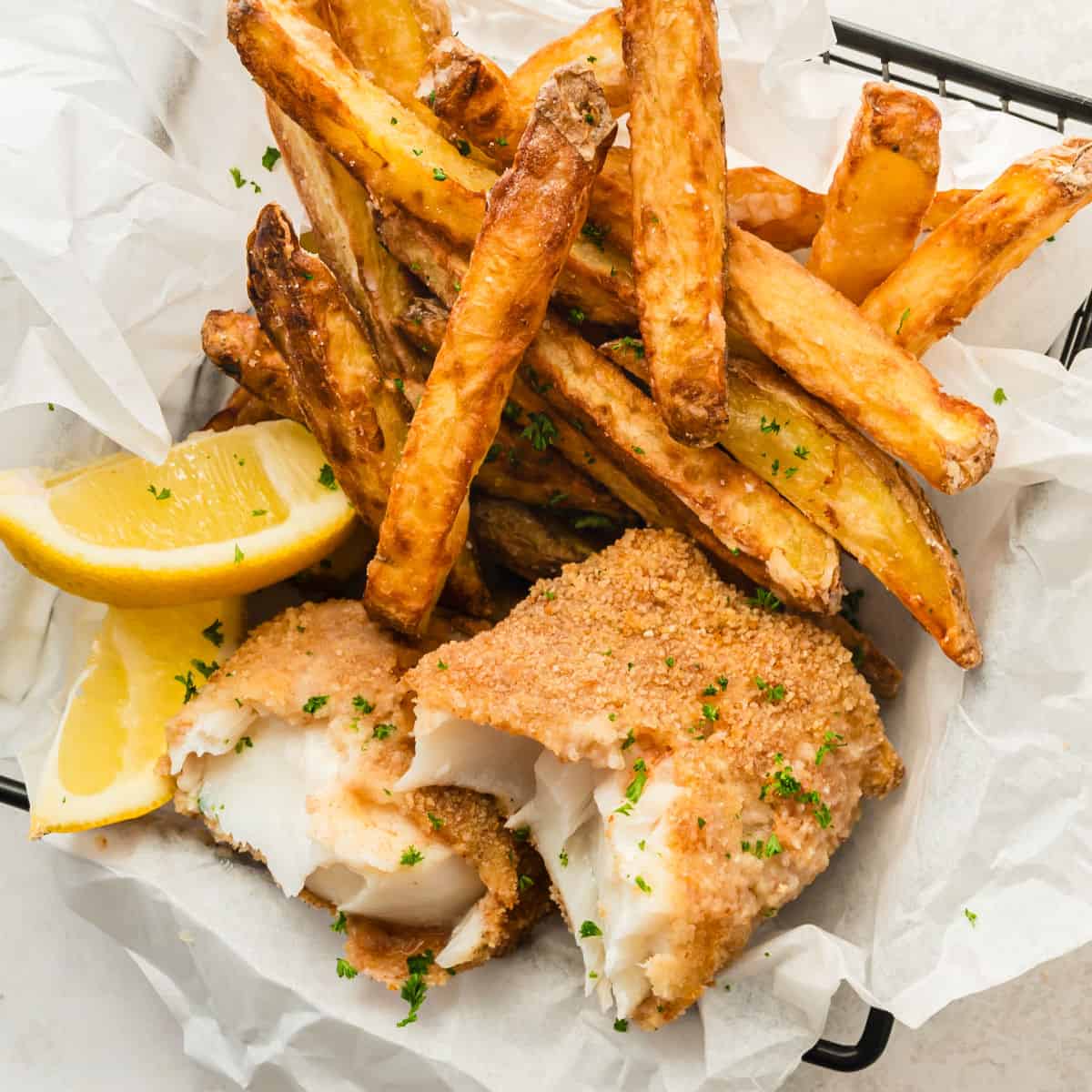 square image of air fryer fish and chips in a basket with lemon wedges