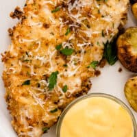 air fryer parmesan crusted chicken breast on a plate with honey mustard with recipe name at the bottom