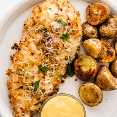 square image of air fryer parmesan crusted chicken on a plate with roasted potatoes and dipping sauce