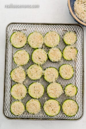 zucchini slices topped with panko and parmesan mixture in an air fryer basket