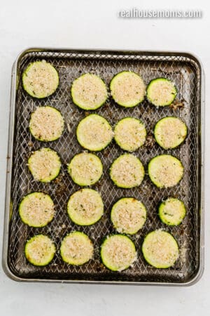 par cooked air fryer parmesan zucchini in an air fryer basket after being flipped and topped with more parmesan breadcrumbs