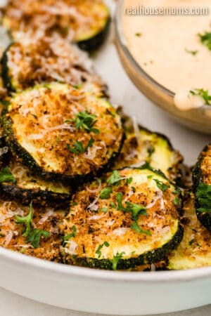 close up of air fryer parmesan zucchini chips on a plate next to a bowl of dipping sauce